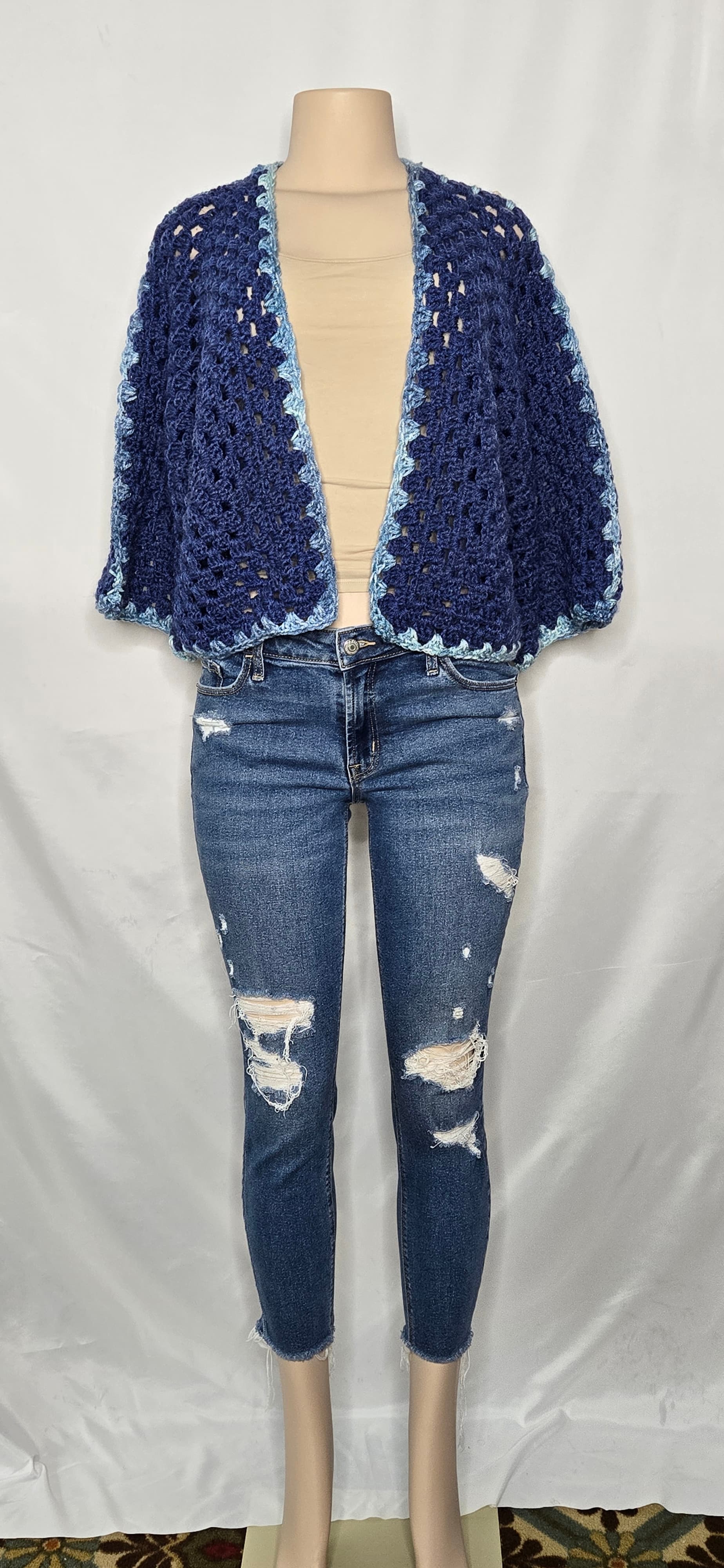 Blue crocheted cape shown from the back on a mannequin
